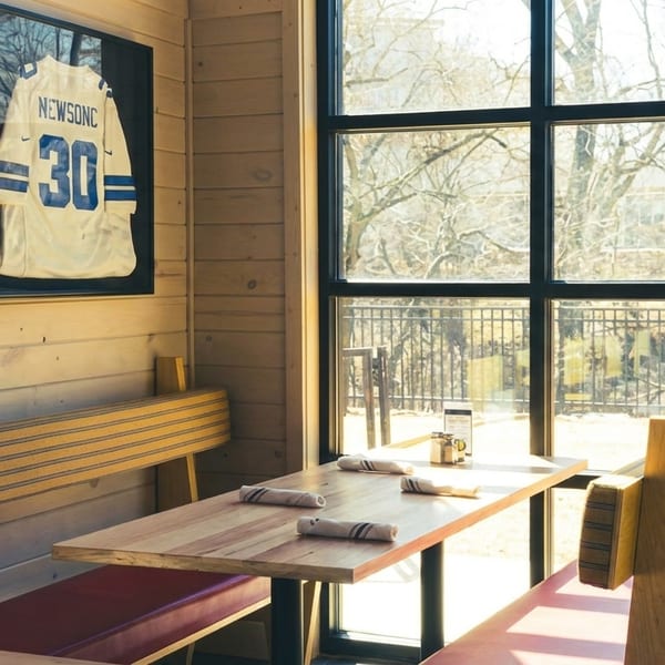 A restaurant booth with wooden benches, red cushions, and a framed sports jersey on a wood-paneled wall.