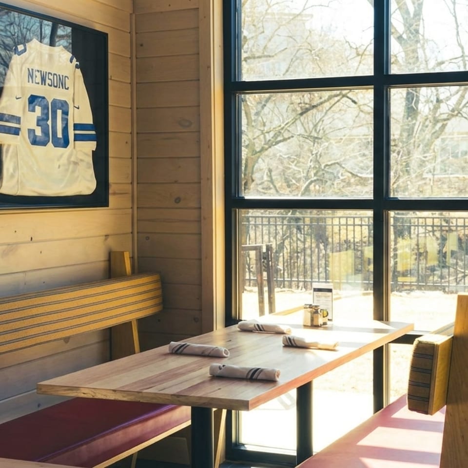A restaurant booth with wooden benches, red cushions, and a framed sports jersey on a wood-paneled wall.