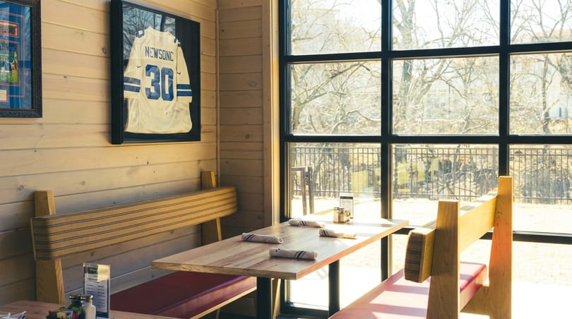 A restaurant booth with wooden benches, red cushions, and a framed sports jersey on a wood-paneled wall.