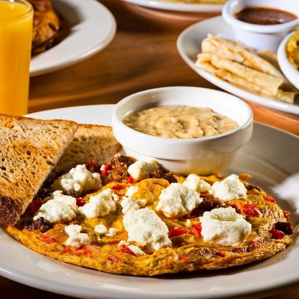 Breakfast spread with an omelet, toast, gravy, orange juice, and another omelet in the background.