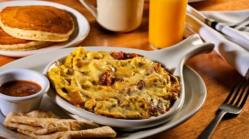 Breakfast skillet with melted cheese, salsa, tortillas, pancakes, orange juice, and coffee.