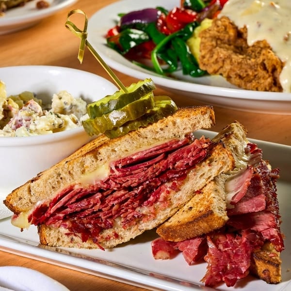 Pastrami sandwich with potato salad, fried chicken, vegetables, and a can of IPA beer.