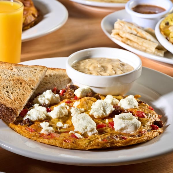 A breakfast omelet with ricotta cheese, toast, and a side of gravy, with orange juice.
