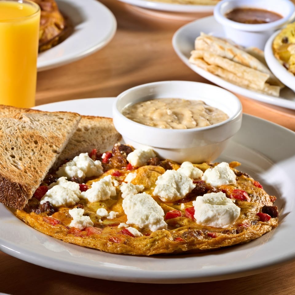 A breakfast omelet with ricotta cheese, toast, and a side of gravy, with orange juice.