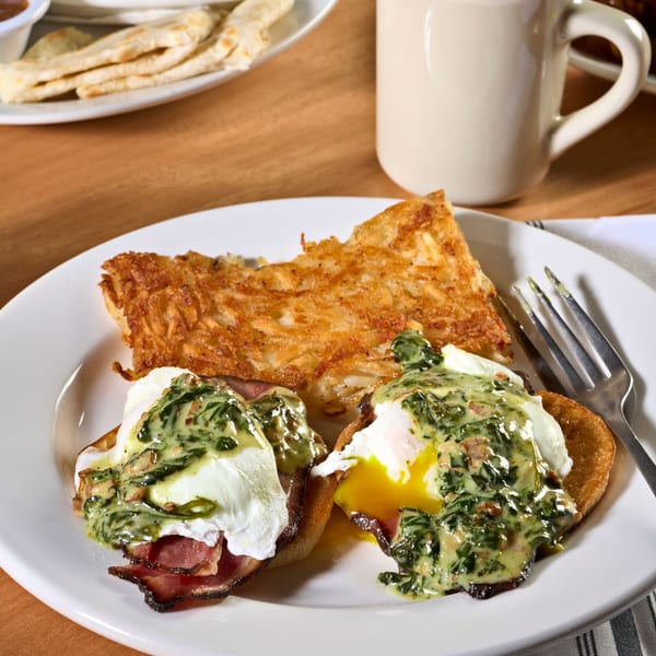 Eggs Benedict with hash browns, coffee, and other breakfast dishes on a wooden table.
