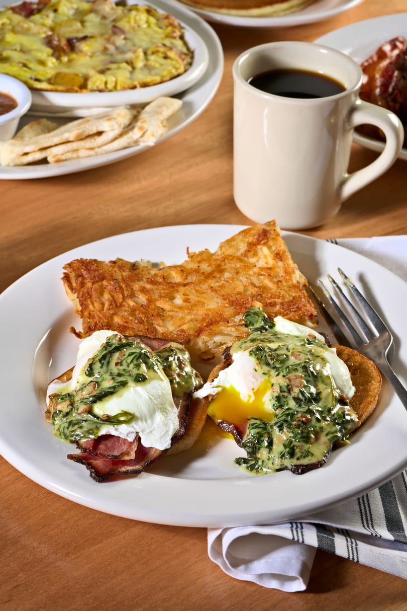 Eggs Benedict with hash browns, coffee, and other breakfast dishes on a wooden table.