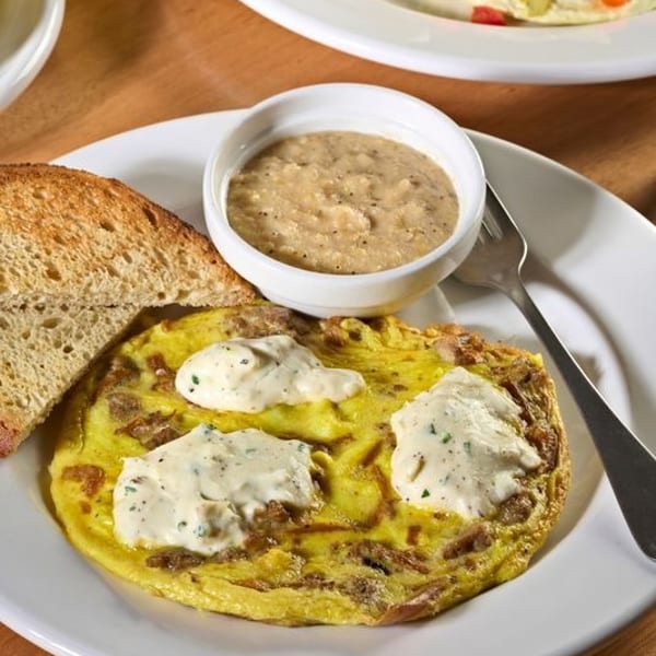 Omelet topped with white sauce, served with toast and a side of grits on a white plate.