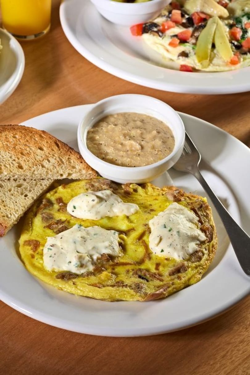 Omelet topped with white sauce, served with toast and a side of grits on a white plate.