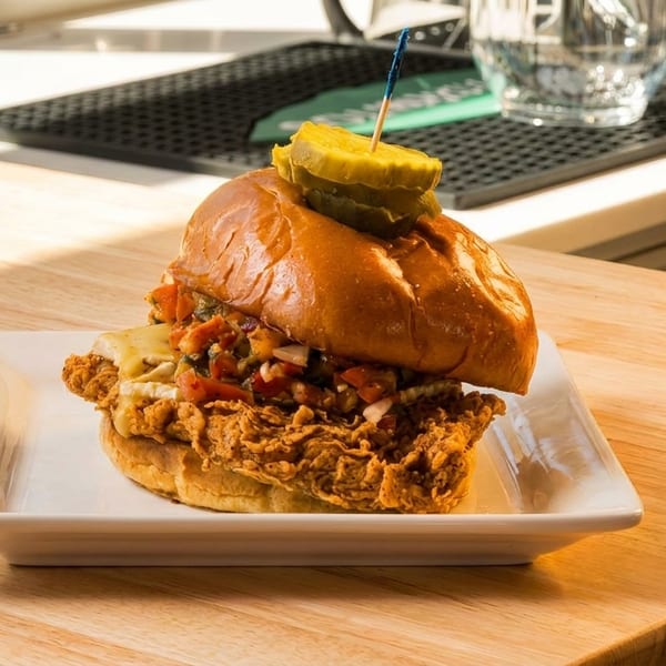 Crispy fried chicken sandwich with melted cheese, salsa, and pickles on a brioche bun.