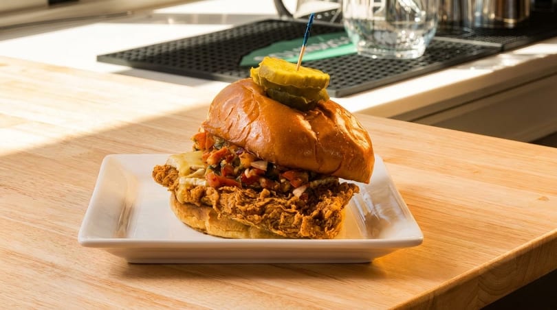 Crispy fried chicken sandwich with melted cheese, salsa, and pickles on a brioche bun.